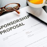Sponsorship proposal form on table with pen, glasses and cup.