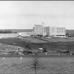 A black-and-white image of a hospital image nestled between rolling hills.