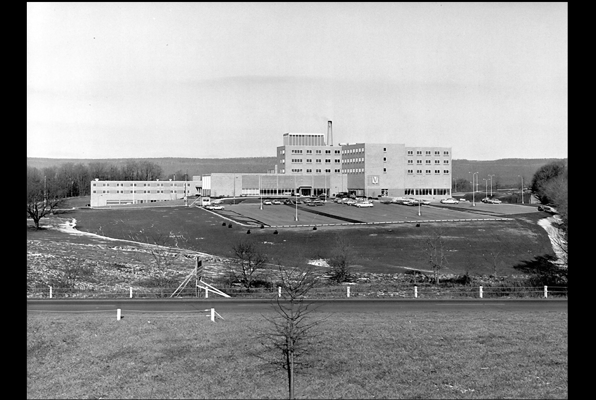 A black-and-white image of a hospital image nestled between rolling hills.