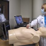 Elizabeth Sinz, MD, associate dean for clinical simulation and director of the Clinical Simulation Center, stands above a mannequin and performs a demonstration during an open house on Sept. 12, 2022.