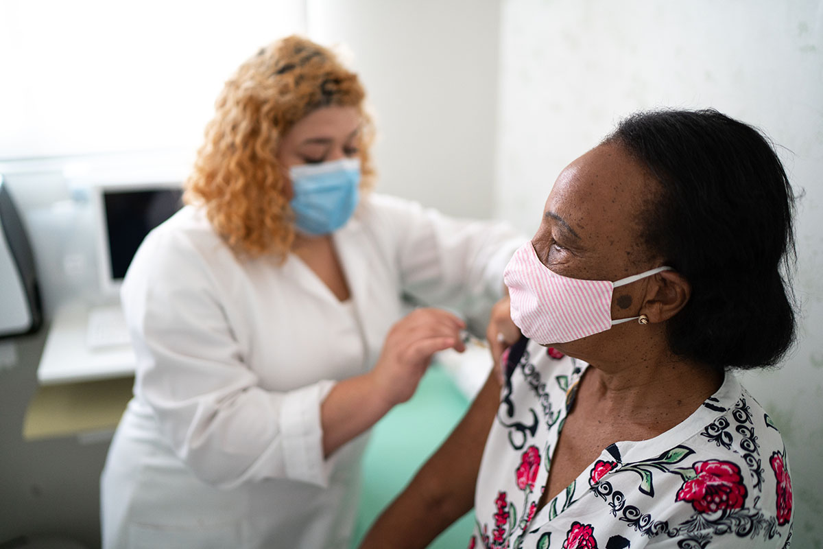 One masked woman provides another masked woman with a vaccine in her right arm.