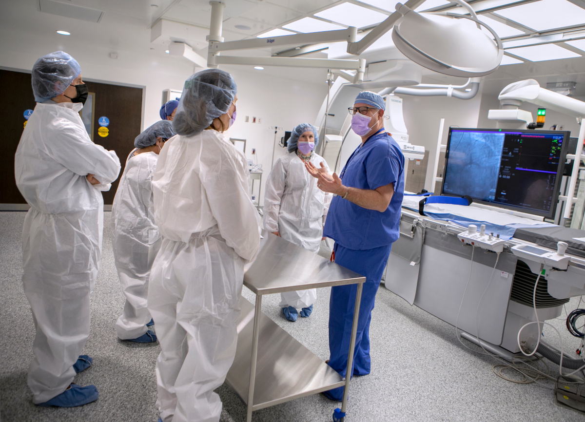 A doctor dressed in scrubs shows several other people a new cardiac catheterization lab