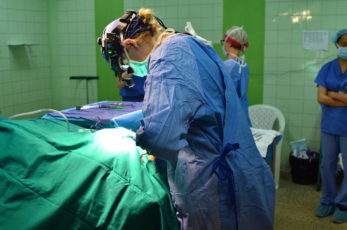 A surgeon works on a patient in an operating room with tile walls.