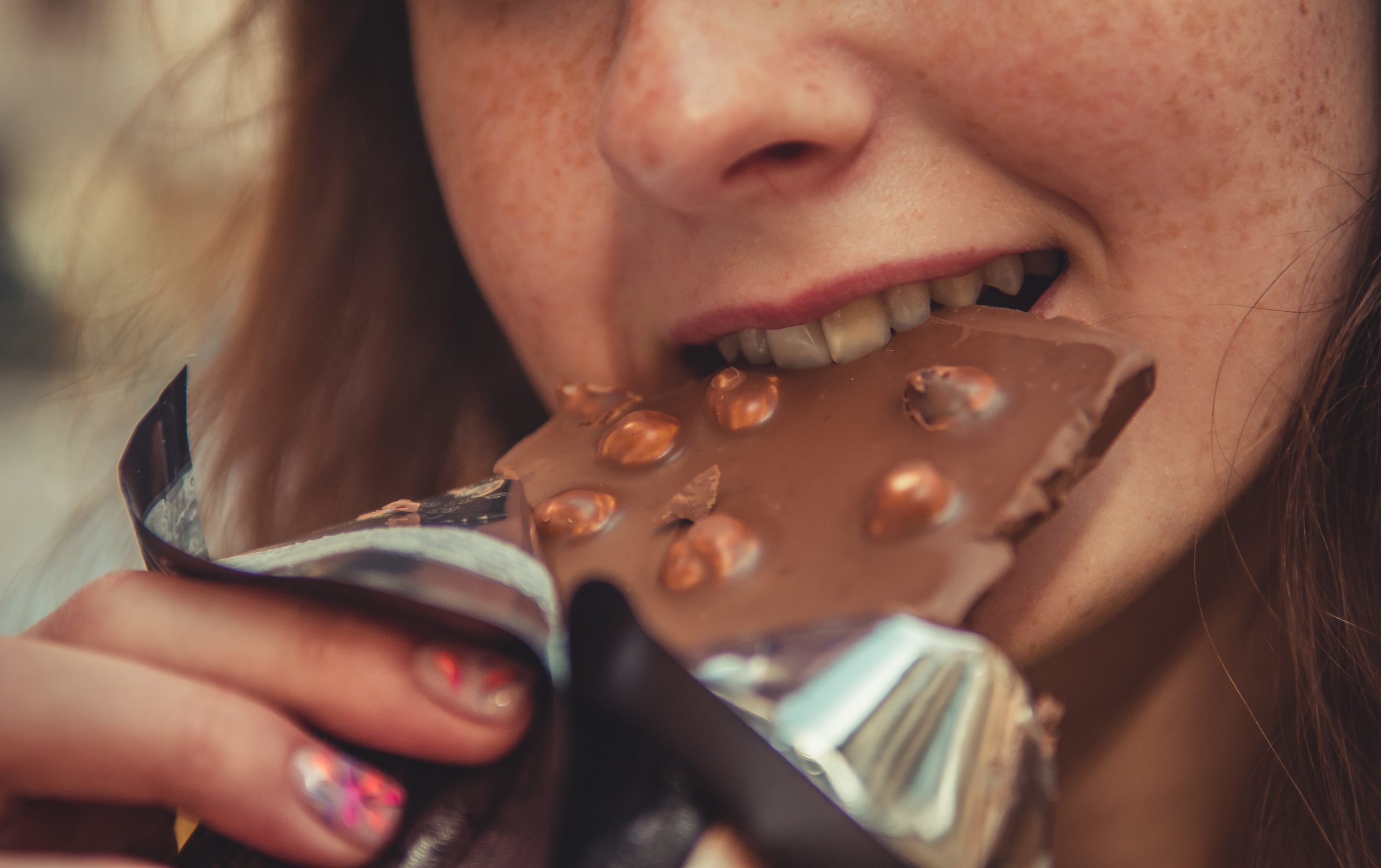 A female adolescent takes a bite of a chocolate bar.