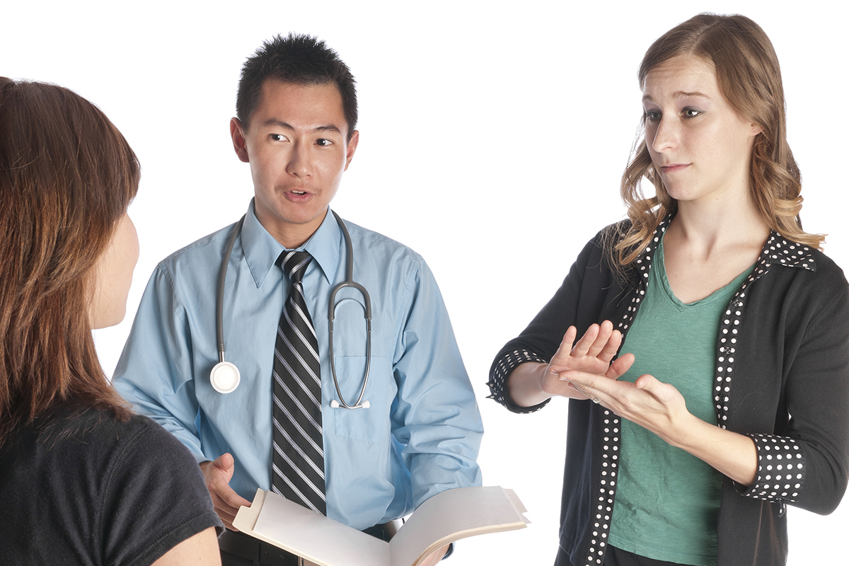 Young woman interpreting for a doctor and woman at the doctor's office using sign language