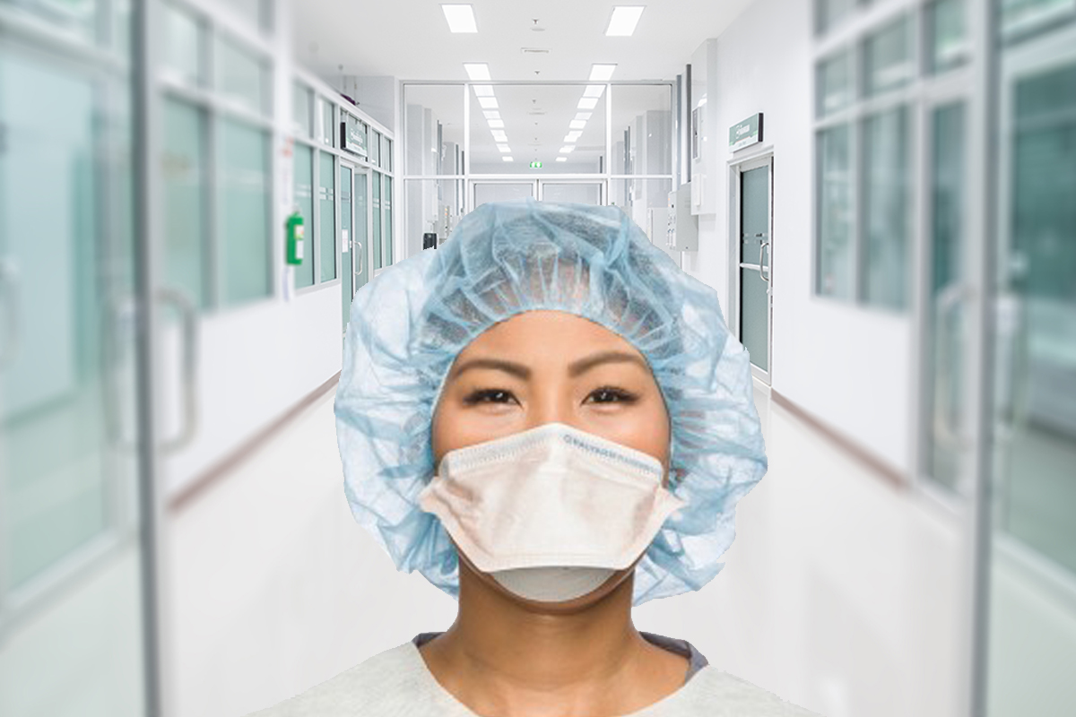 Head shot of female clinician wearing a surgical head cap and N95 mask, hospital doorway and hall in background.