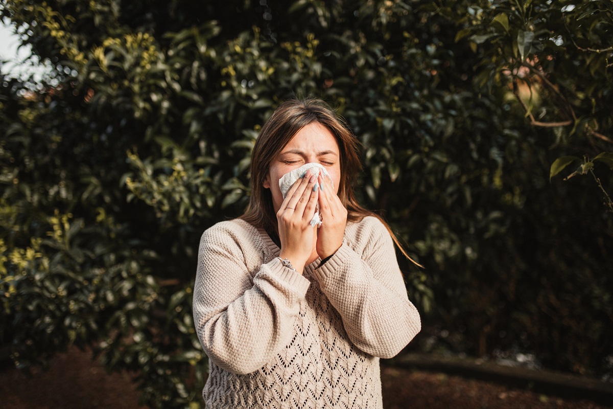 Young woman suffering spring allergy and blowing nose with a tissue.