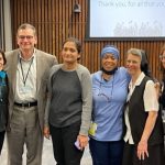 A group of six men and women stand in an auditorium.