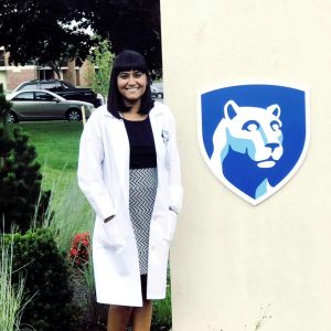 Ashna Dhoonmoon, wearing a laboratory coat, stands beside the Penn State logo. 