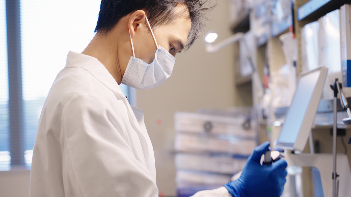 Jiaxing Chen, a bioinformatics and genomics doctoral student at Penn State College of Medicine and Penn State Huck Institutes of the Life Sciences, pipettes a solution in a laboratory while wearing gloves, a lab coat and a mask.