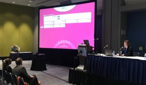 Dr. Jonathan Stine sits on a podium beside a large projector screen and moderates a session during Digestive Disease Week in Chicago, Illinois. 