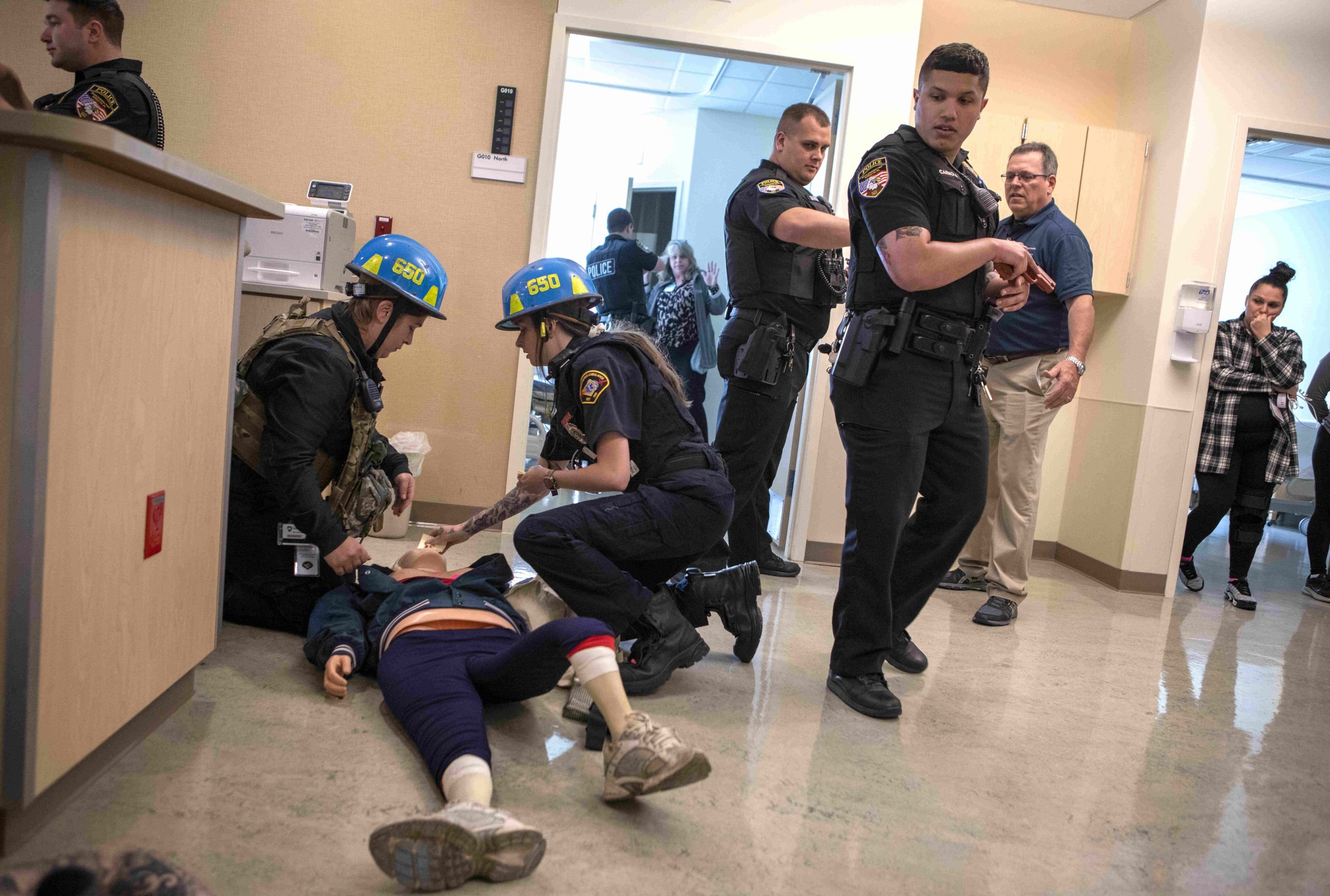 Two first responders attend to a mannequin – a simulated victim – while police officers and other drill participants look on.