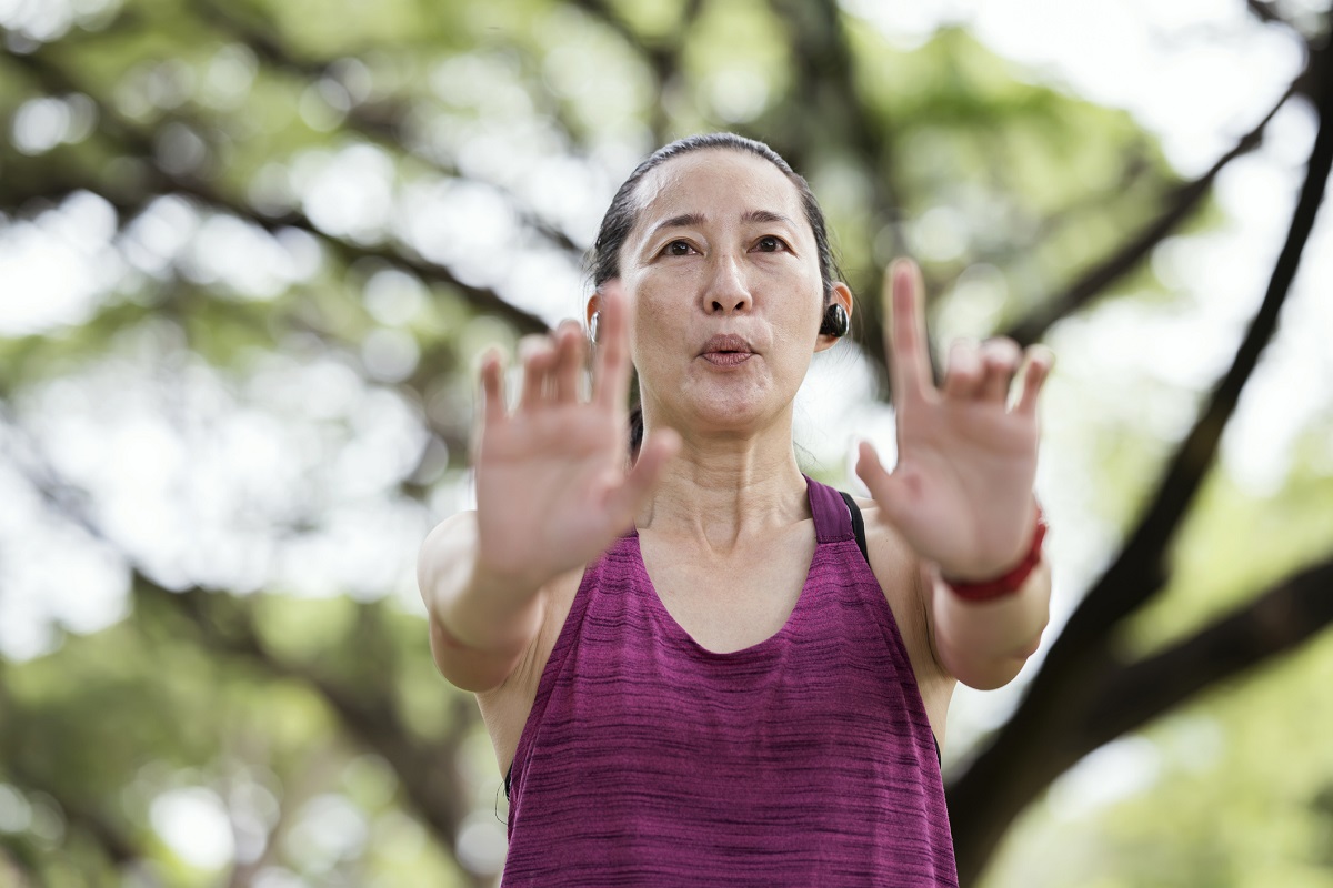 A woman practices qigong poses in a park.
