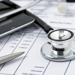 Digital tablet, pen and stethoscope laying on medical financial statement