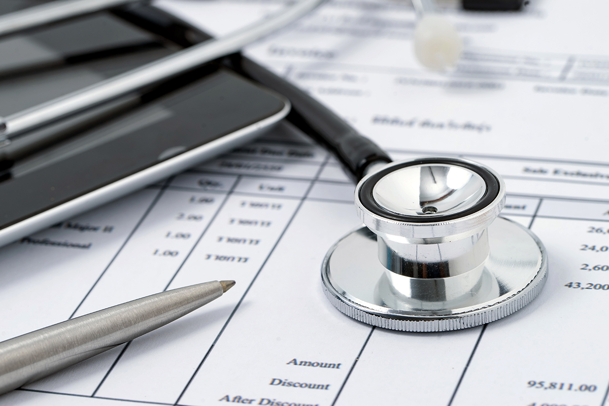 Digital tablet, pen and stethoscope laying on medical financial statement