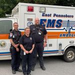 Three individuals in emergency medical personnel uniforms standing in front of an East Pennsboro Township ambulance.