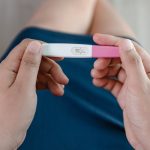 Close-up of a woman’s hands holding a pregnancy test kit and waiting for positive result in her bedroom.