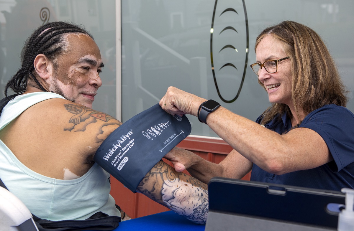 A man receives a blood pressure screening from a woman. Both smile.