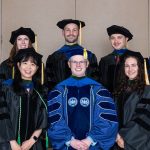 Nine people pose for a picture together wearing academic regalia.