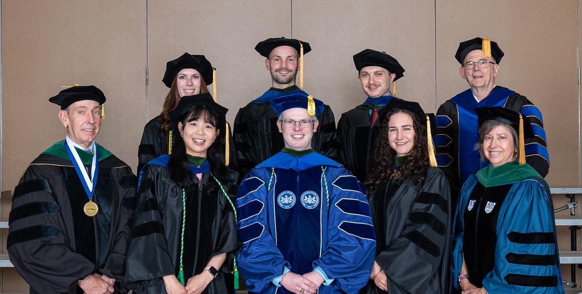 Nine people pose for a picture together wearing academic regalia.