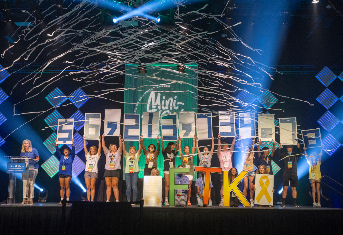 A group of kids hold up signs to reveal a fundraising total of over $6 million.