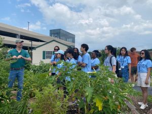 Daniel George, PhD, professor of public health sciences and humanities, stands outside in a garden while he leads the Global Health Exchange Program group on a tour of the community garden on the campus of Penn State Health Milton S. Hershey Medical Center.