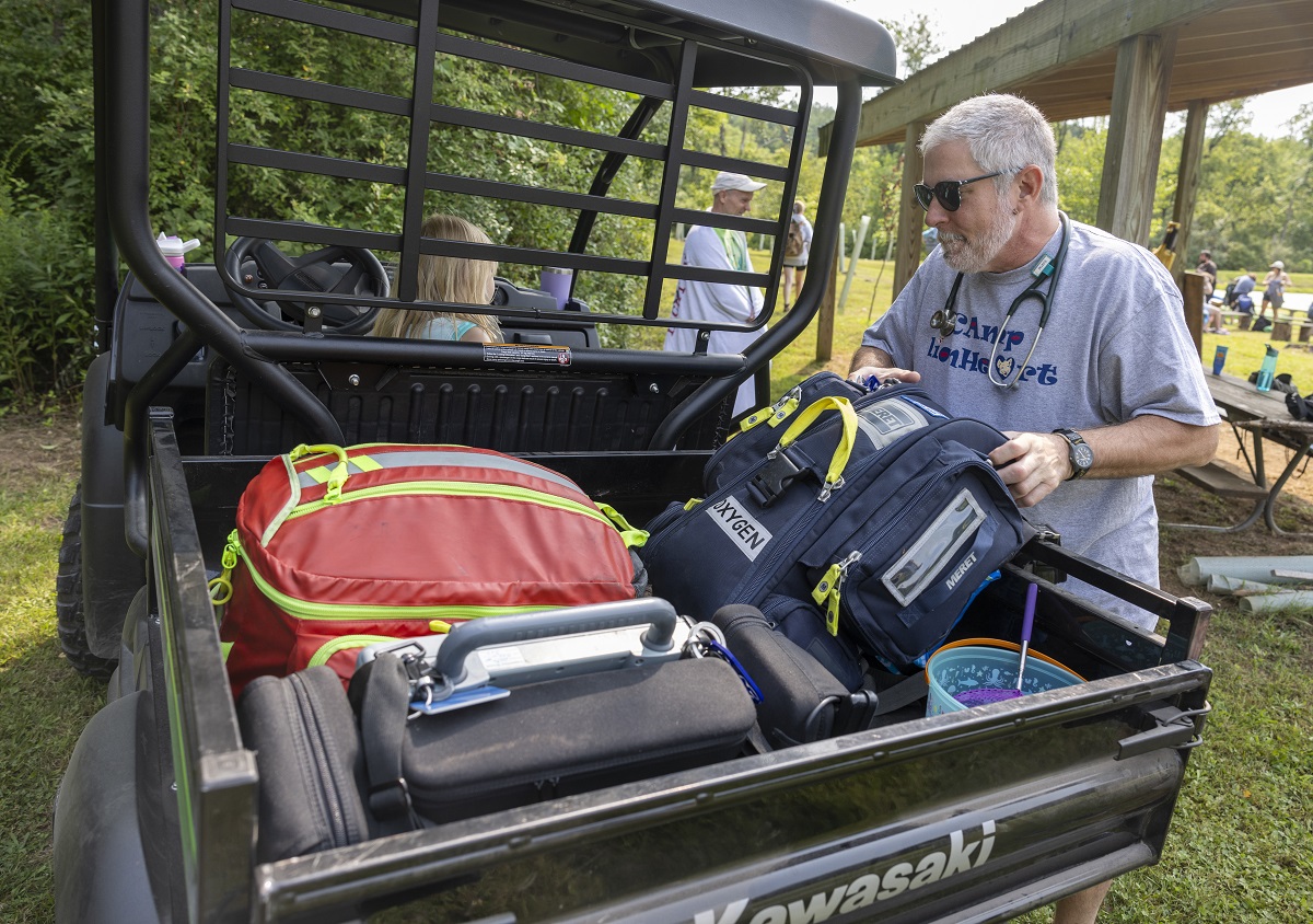 A man places packs in the back of a utility vehicle. He wears a Camp LIonheart T-shirt.