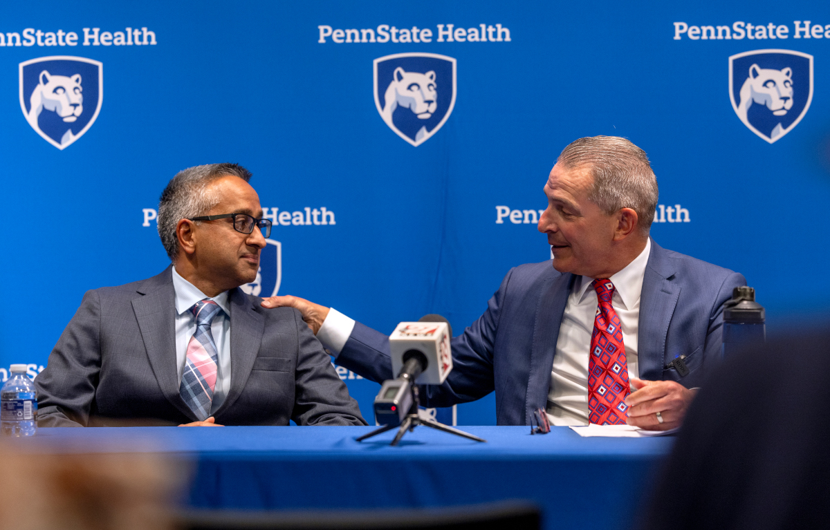 Two men in suits sit next to each other, talking and smiling