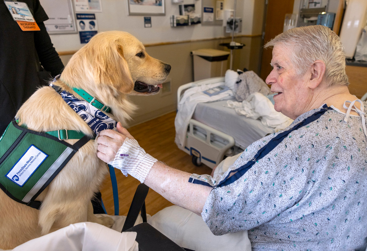 A man in hospital gown pets and smiles at a golden retriever