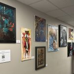 A man stands near a collection of paintings on a wall.