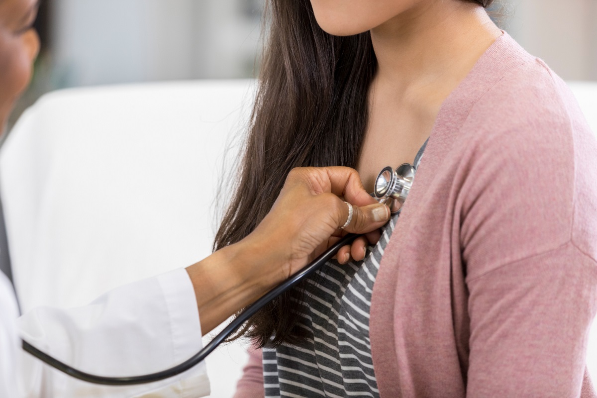 A doctor listens to a young woman’s heartbeat with a stethoscope.