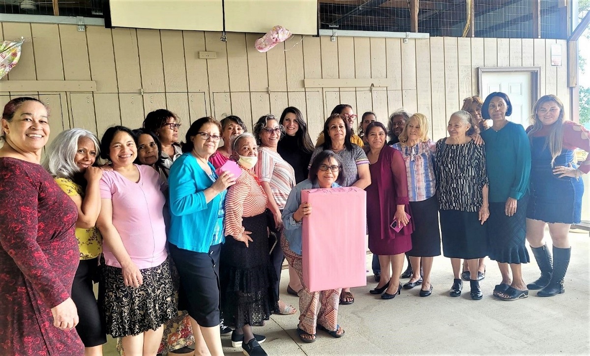 Twenty-one women stand together at a breast cancer education event. 