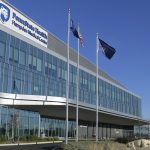 Hospital building with large, reflective windows on most of the exterior, a sign that says, “Penn State Health Hampden Medical Center” with a shield containing the image of a mountain lion – The Penn State Nittany Lion. Three flags in front of the building – American, Pennsylvania, Penn State Health. Nittany Lion statue in the foreground.