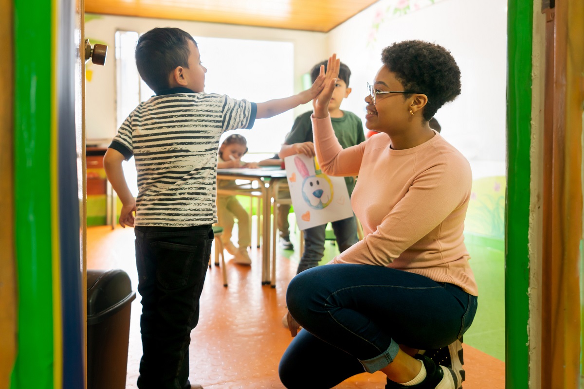 Happy African American preschool teacher high fiving a student entering the classroom - back to school concepts