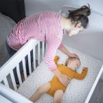 A mother puts her baby to sleep in a crib.