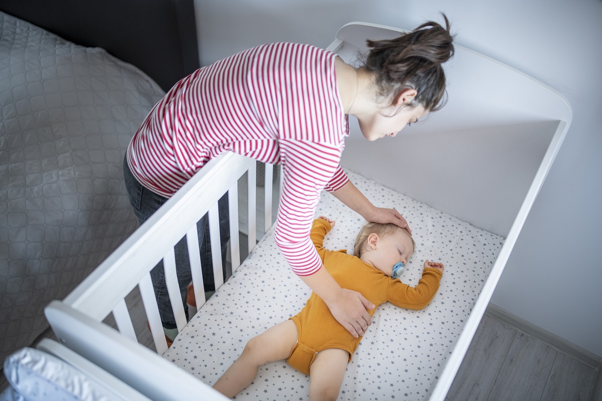 A mother puts her baby to sleep in a crib.