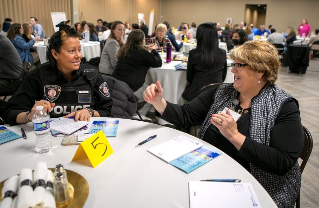 Two women, one wearing a police uniform, sit together and have a conversation. 
