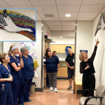 A woman points to art featuring good while several health care workers look on.