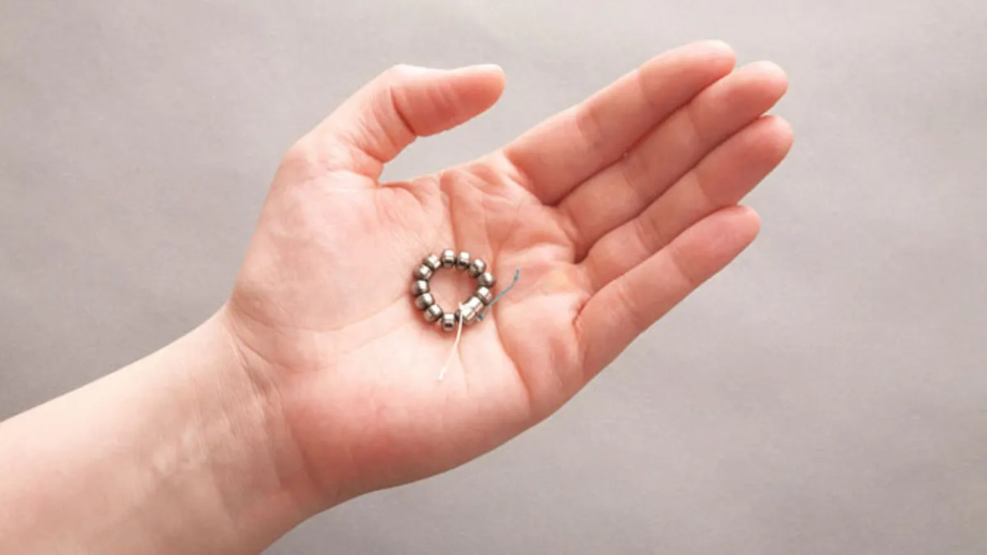 A hand holding the LINX device, a small band of magnetic titanium beads