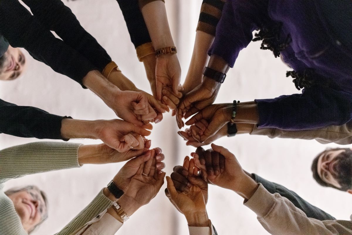 View from below of several people standing in a circle, putting their hands together in the center.