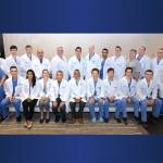 A group of men and women in white coats and surgical scrubs pose for a photo.