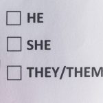 Red felt-tip pen hovering over a piece of paper with checkboxes next to “he,” “she” and “they/them.”