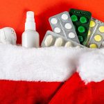 Close-up of pills, thermometer and antiseptic in santa hat on red background