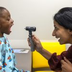 A physician uses a light to check the throat of a child.
