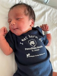 A newborn baby lays down while wearing a t-shirt with the Penn State Health St. Joseph logo.
