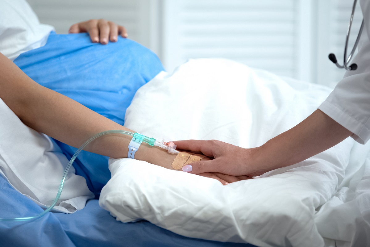 A doctor holds a pregnant woman's hand in a hospital bed.