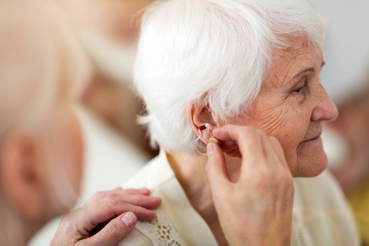 Female doctor applying hearing aid to senior woman's ear.