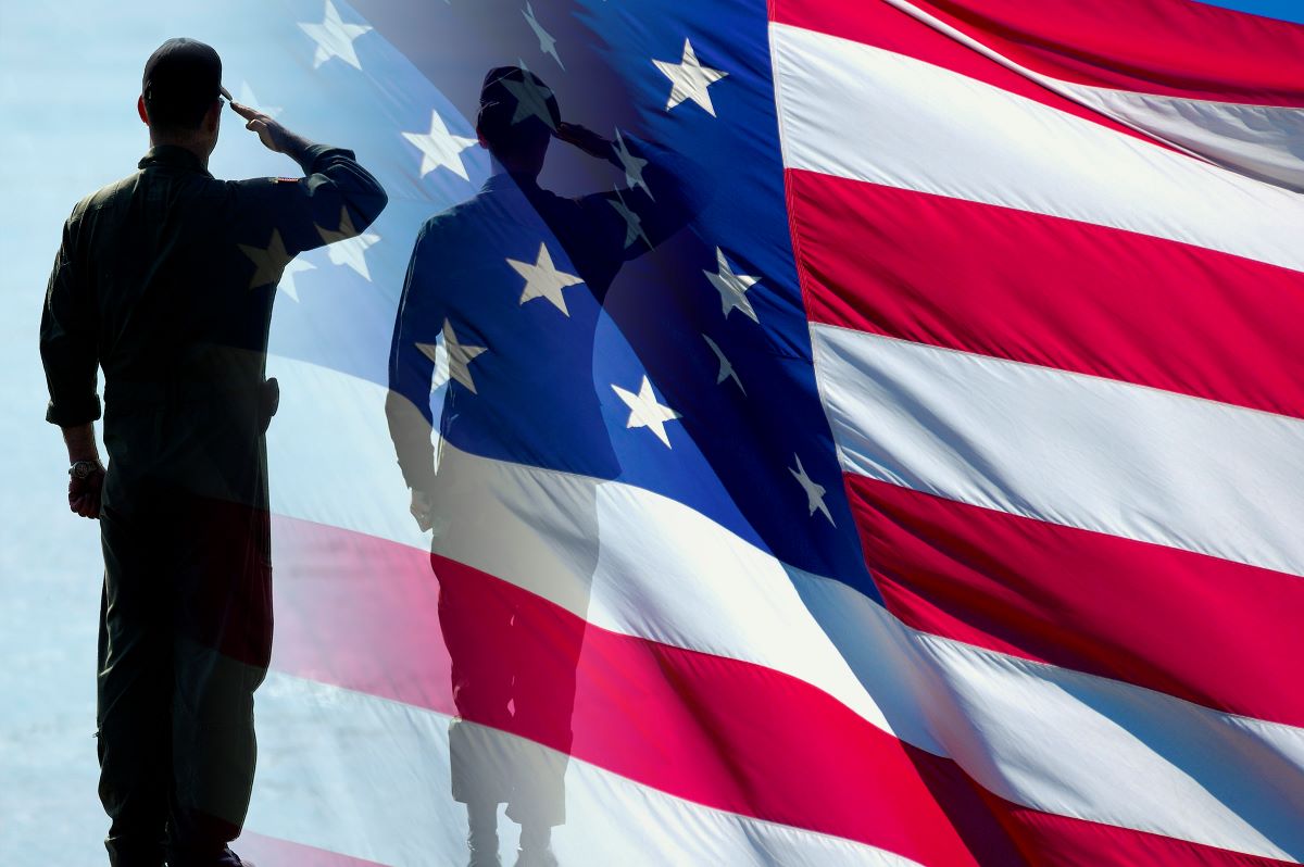 A soldier in casual uniform, facing away, saluting. Waving American flag fills the background.