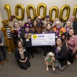 Eighteen people – along with a dog and a costumed Nittany Lion – pose with a check made out to Penn State Health Children’s Hospital in the amount of $112,854, from Spirit of Children. Large gold inflatable numbers spelling out “1,000,000” are on the wall directly behind them.