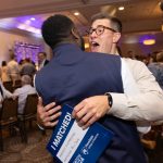 Two matching MD students hug, the one whose face can be seen has a joyful expression and holds an 'I Matched!' card